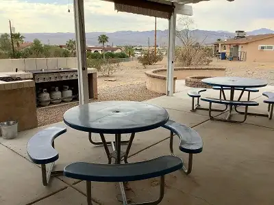 view of the backyard, showing two picnic tables, a BBQ and a fire pit
